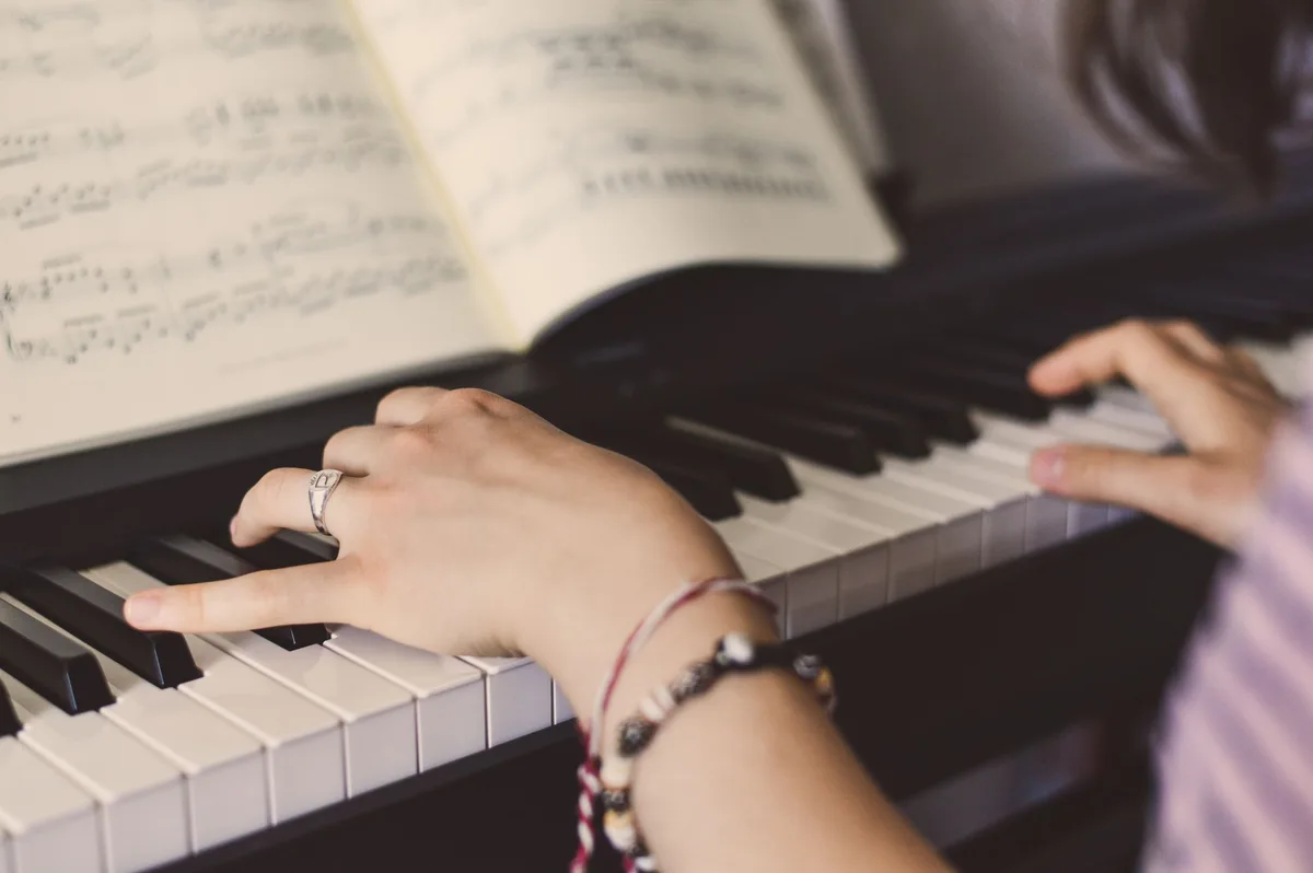 Close view of both hands at a piano with an open score above the keyboard