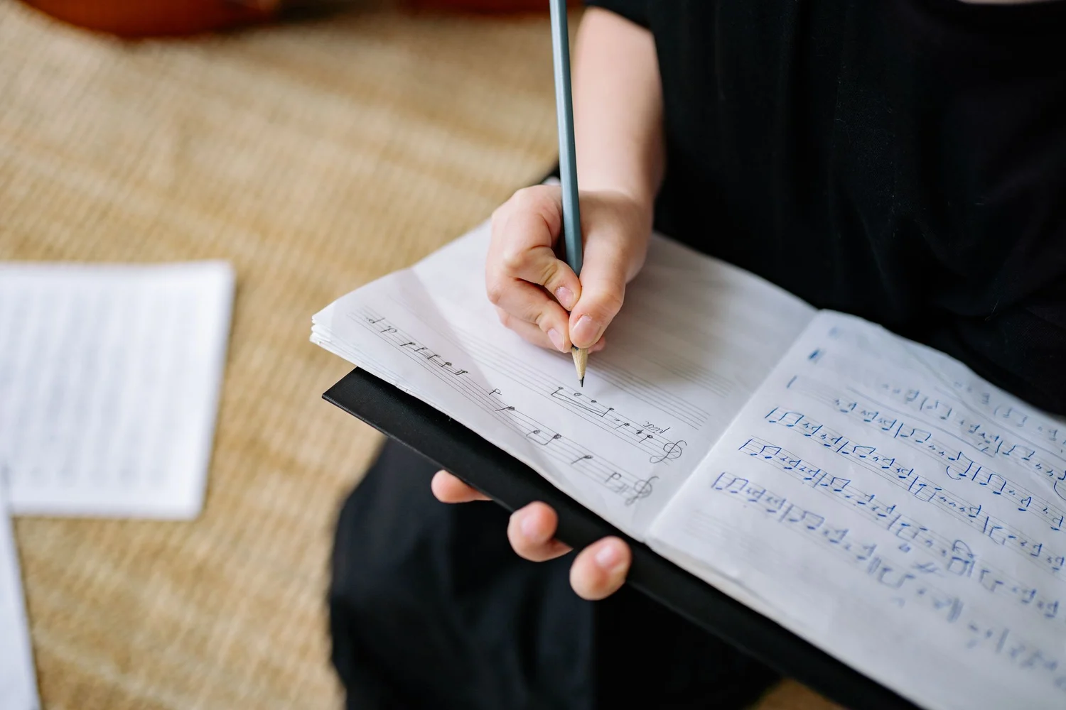 A hand writing musical notation with a pencil in a manuscript notebook