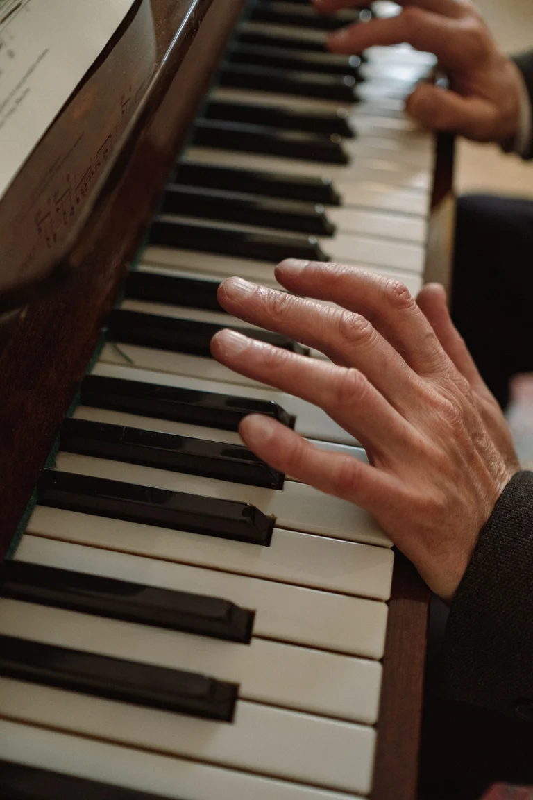 Close-up of a pianist’s hands on an upright piano keyboard, with a score above