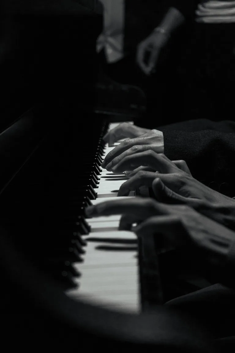Two pianists’ hands sharing a keyboard in a black-and-white close-up