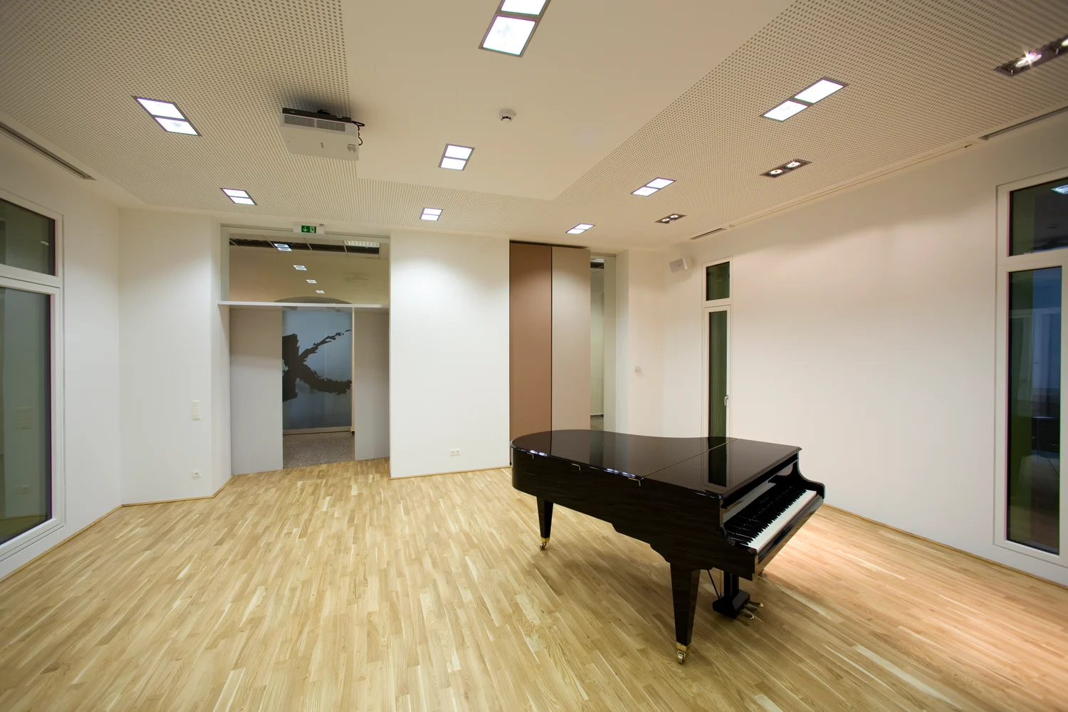 Grand piano in MUK’s Turmraum 1 at Johannesgasse 4a, an empty room with a wooden floor and acoustic ceiling