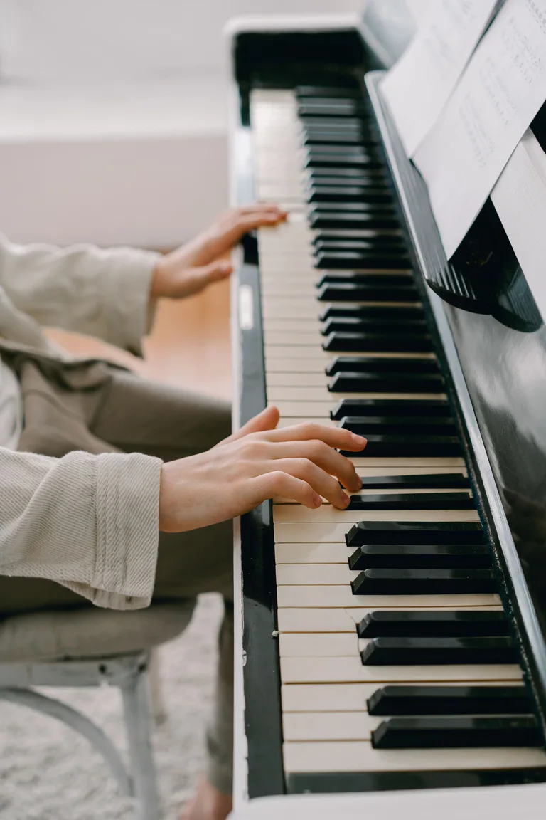 Hands at an upright piano beneath an open score