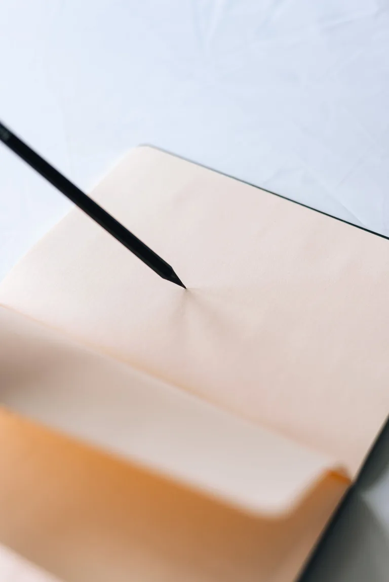 A dark pencil resting against a blank page of an open notebook