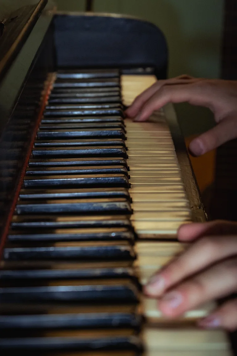 Close-up of two hands playing the worn keys of an upright piano
