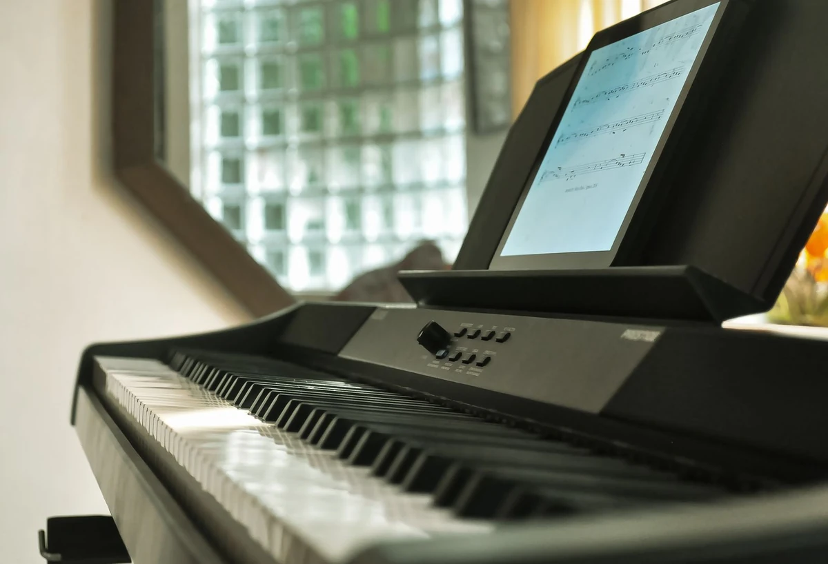 A digital piano beside a window, with a score displayed on a tablet above the keys