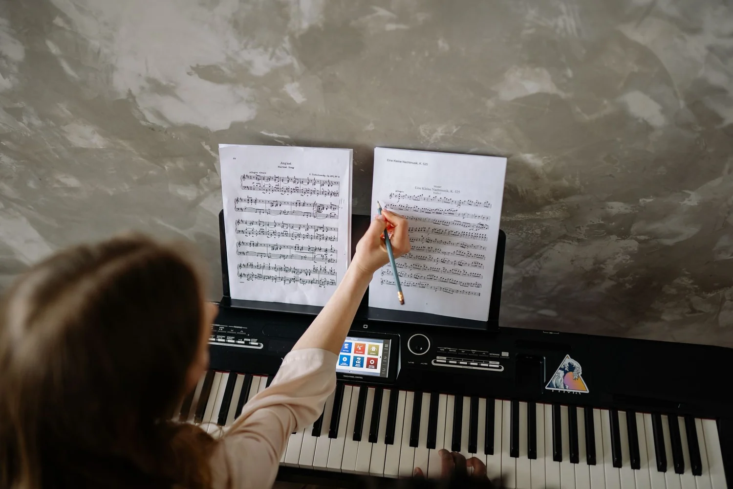 A pianist seen from behind marking a score with a pencil at a digital keyboard