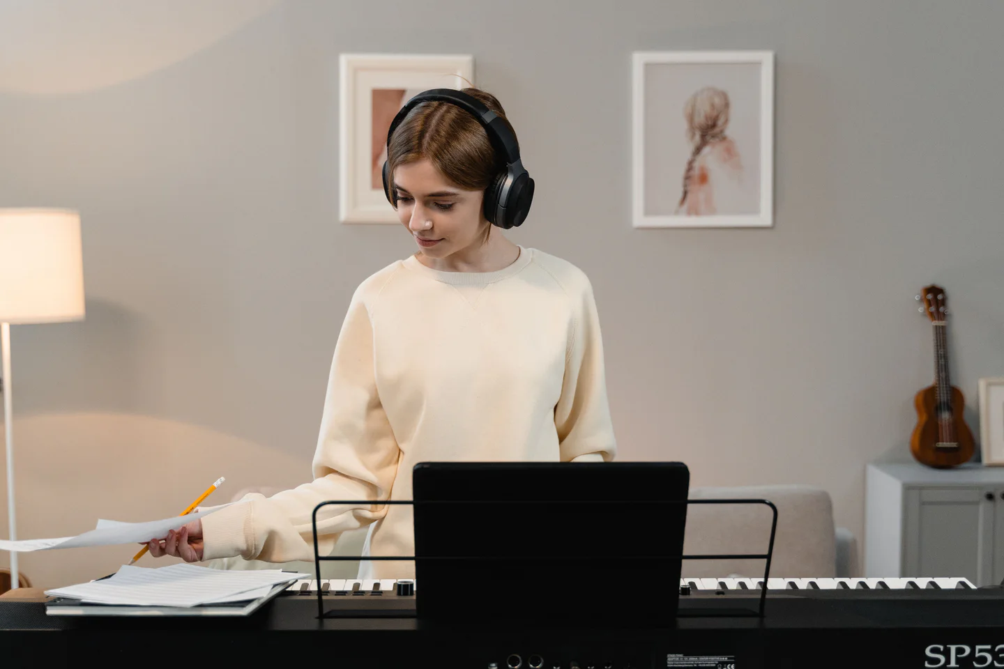 An adult wearing headphones and holding music beside an electronic keyboard.