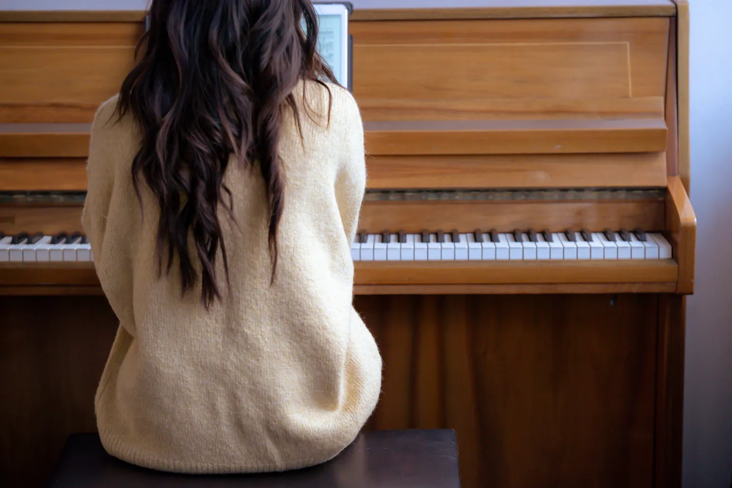 Adult pianist reading music from a tablet at an upright piano.