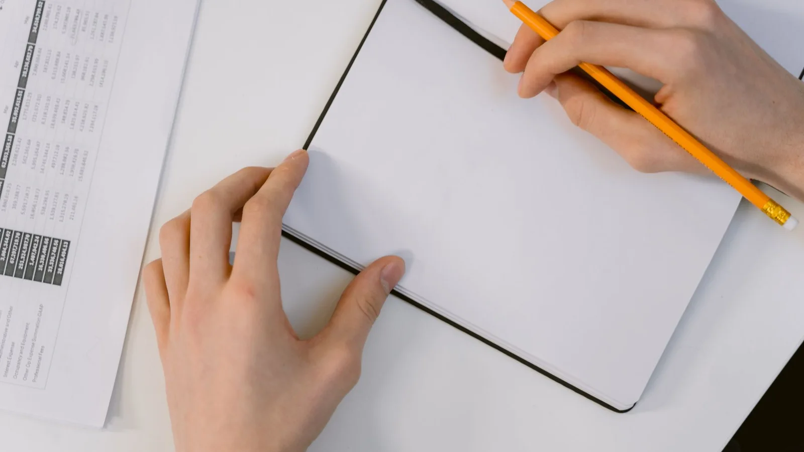 Hands holding a pencil over an open blank notebook