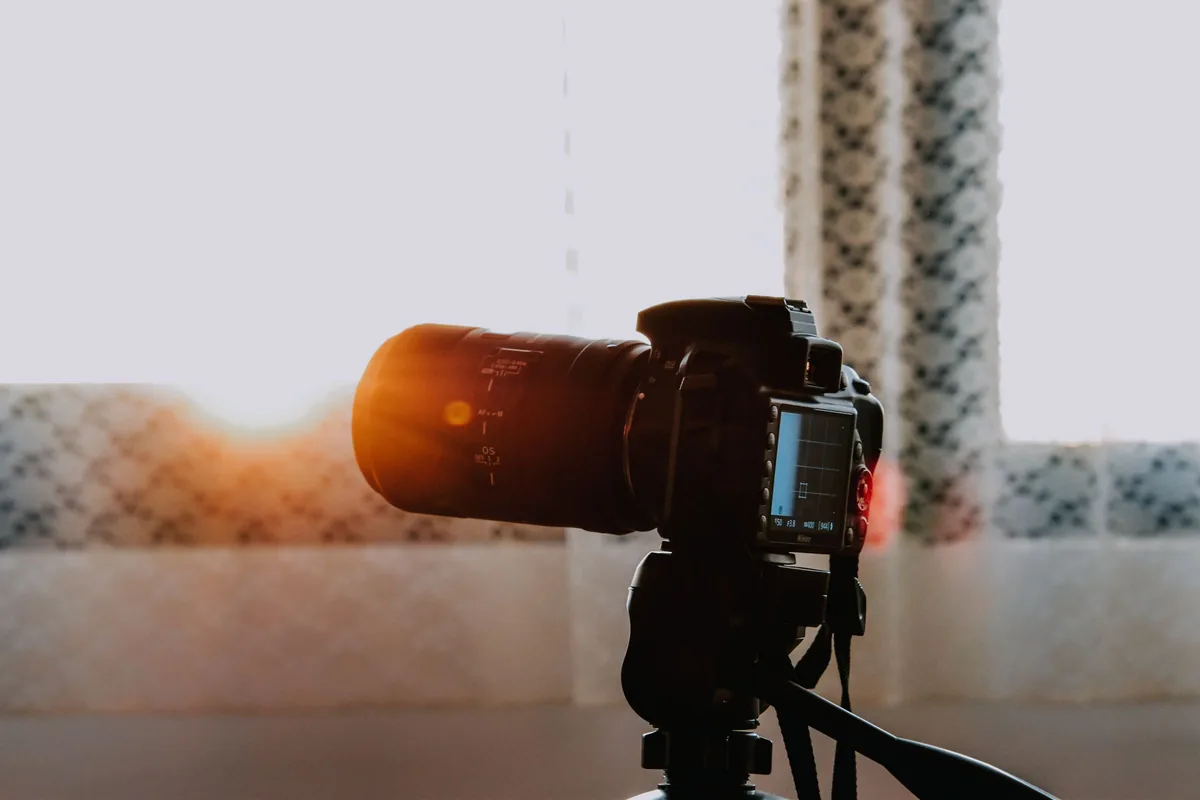 A camera supported on a tripod beside a sunlit window