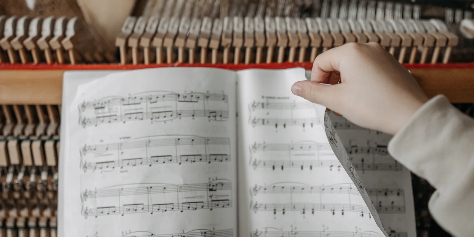 A hand turning a page of music at an upright piano