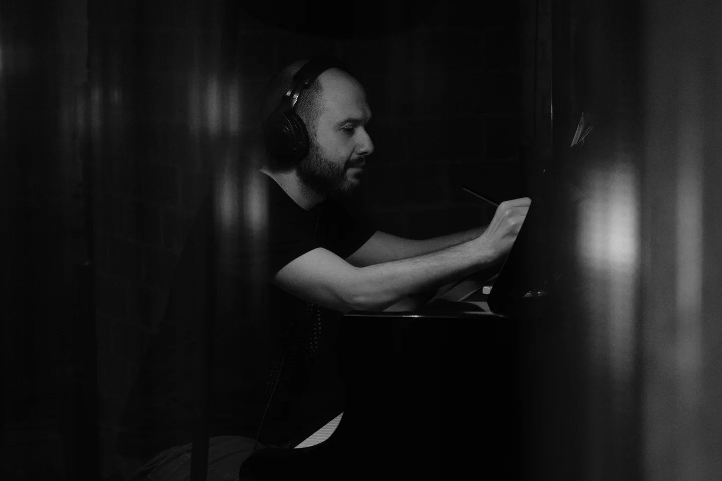 Pianist wearing headphones and writing notes beside a grand piano.