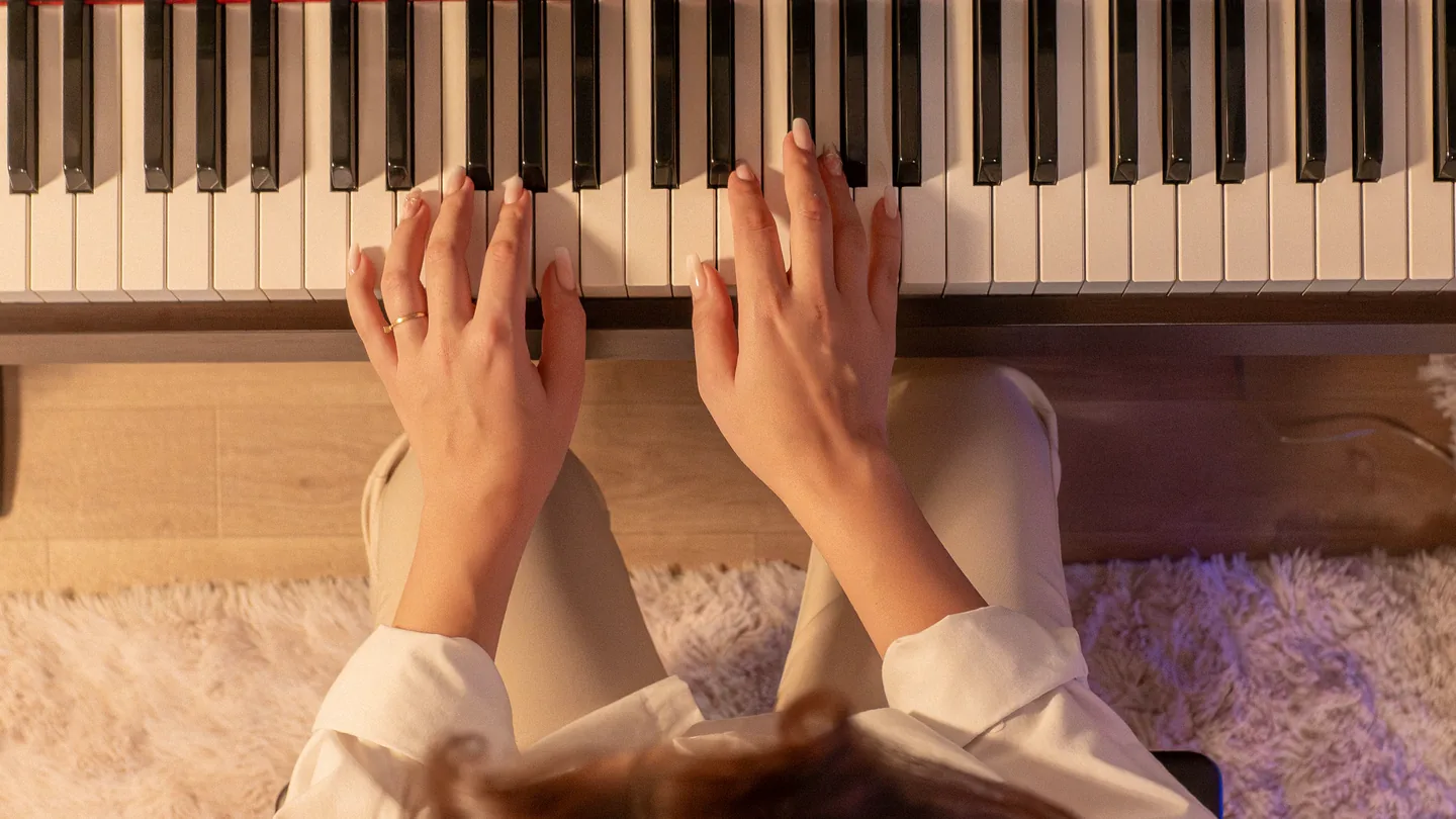 暖色の照明の下、電子ピアノを弾く大人の手元を上から見た写真。