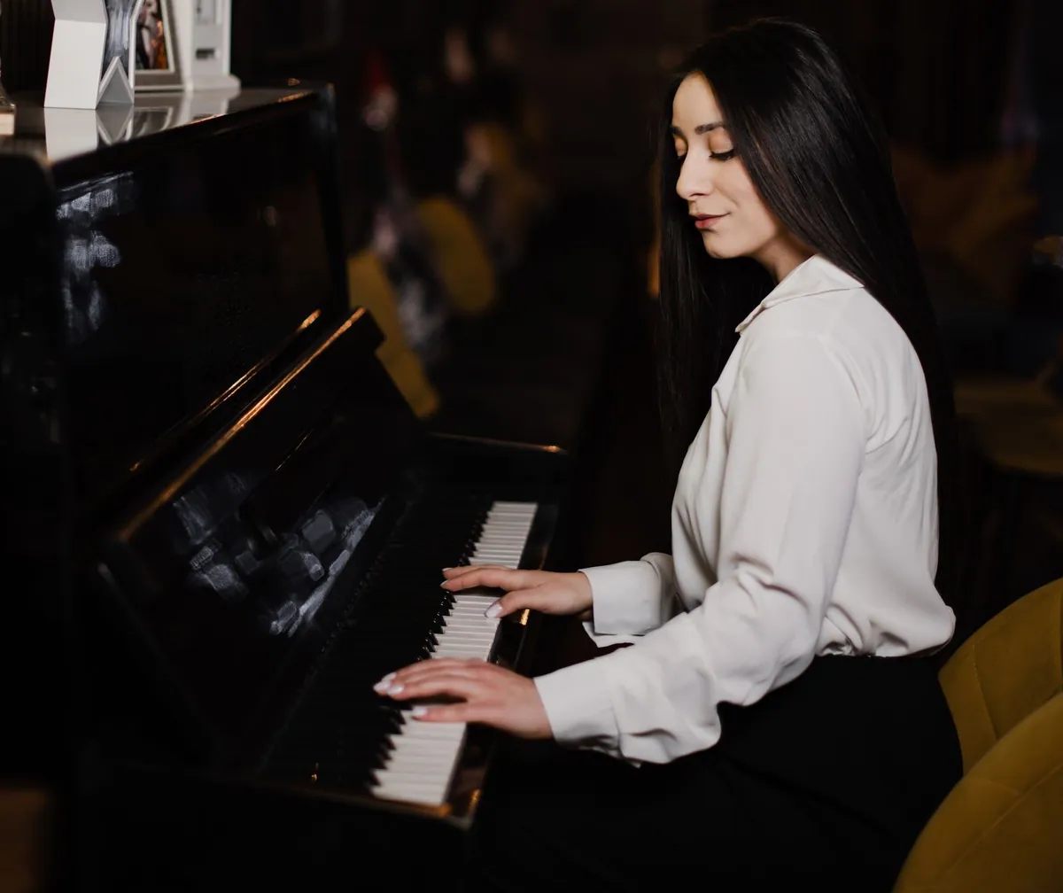 An adult pianist seated at an upright piano in a softly lit room